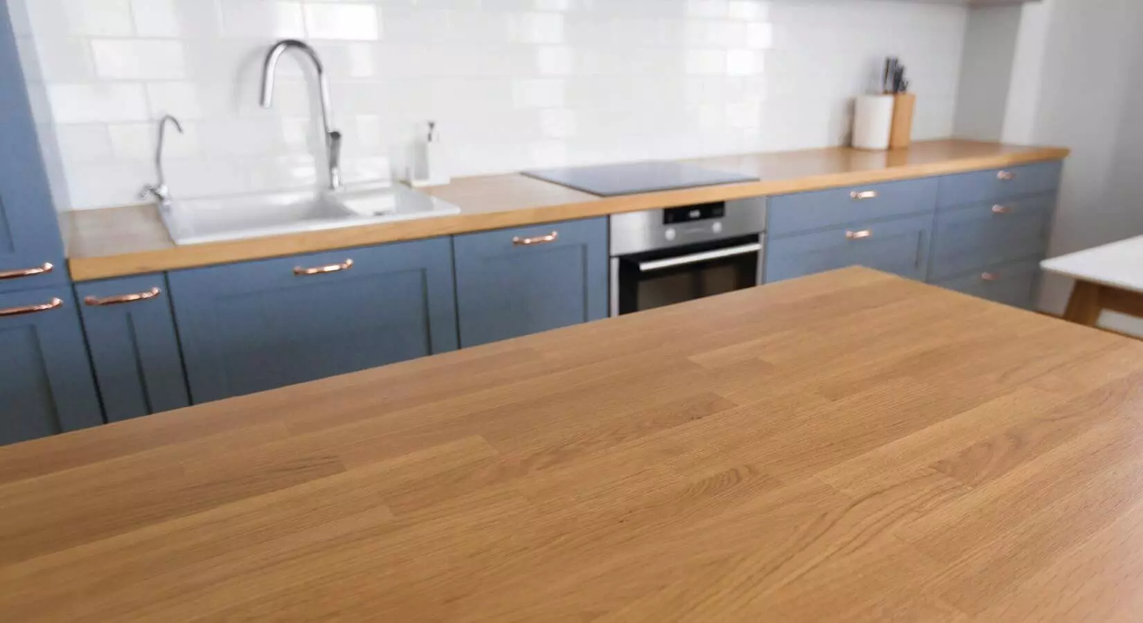 Kitchen with gray-blue cabinets, white tile backsplash, and butcher block countertops.