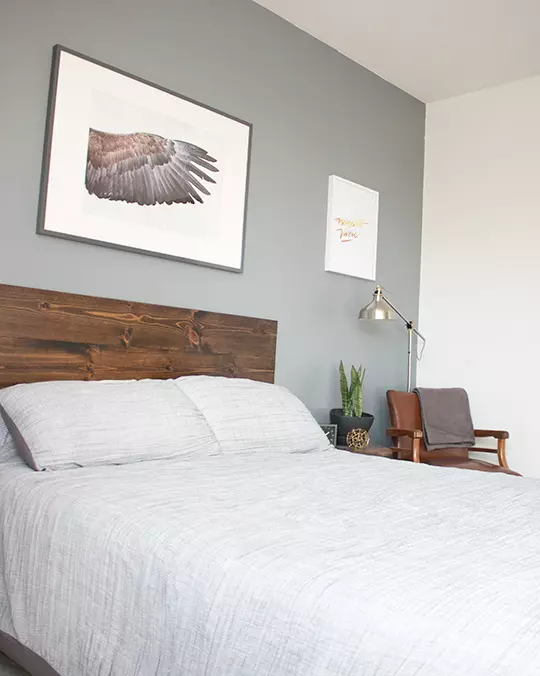 a bedroom area with a bed with a wooden headboard, a side table and chair, and wall decor