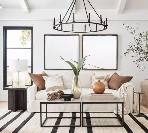 Beautiful slop arm white slipcovered sofa, black chandelier, black coffee tables, and striped rug in neutral modern living room