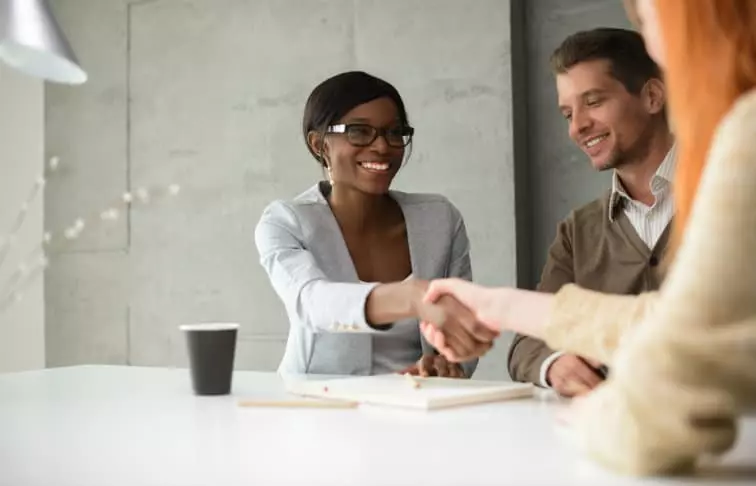 Professionally dressed real estate agent shaking hands with a young couple