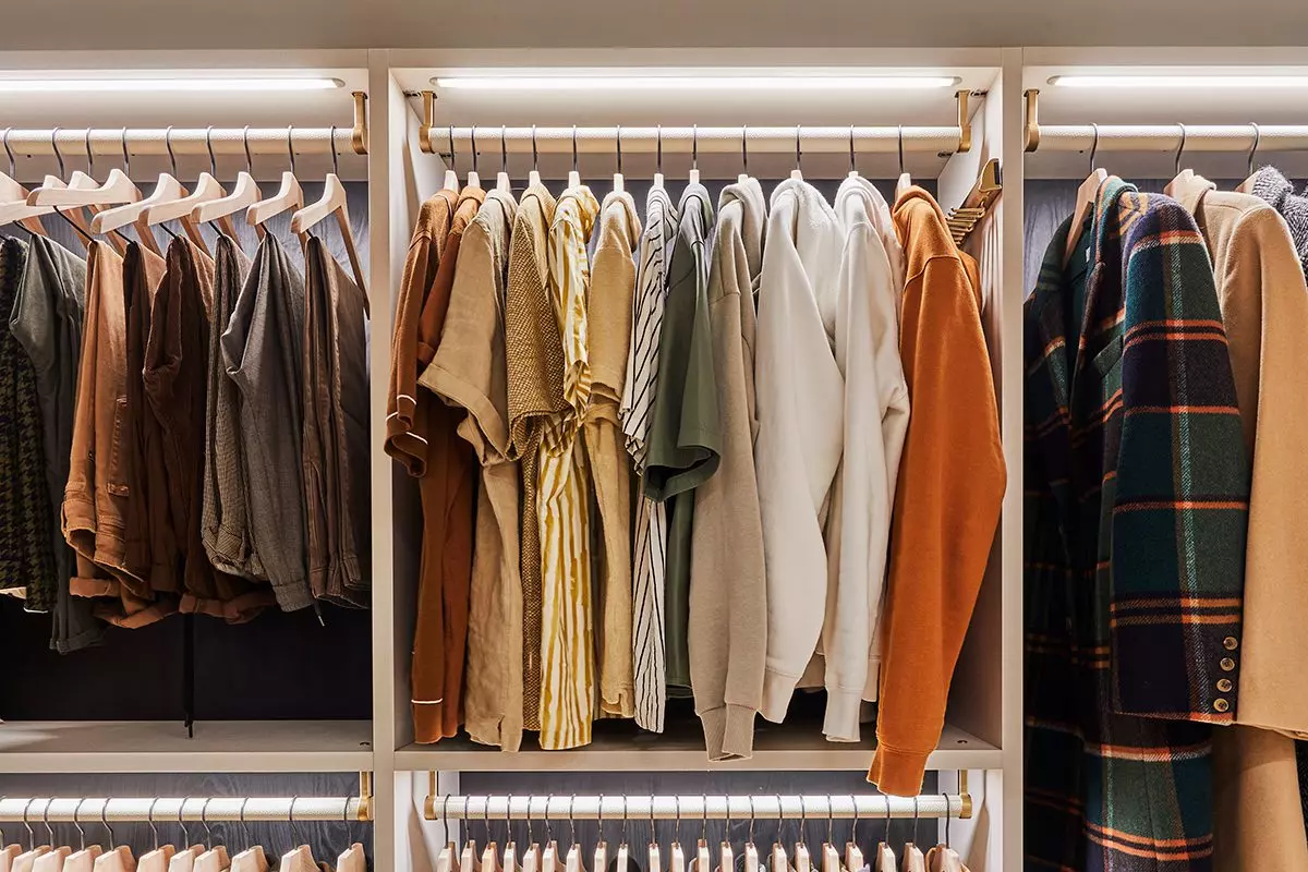 Custom reach-in closet showing clothes ordered by color and category with LED lighting feature created by California Closets