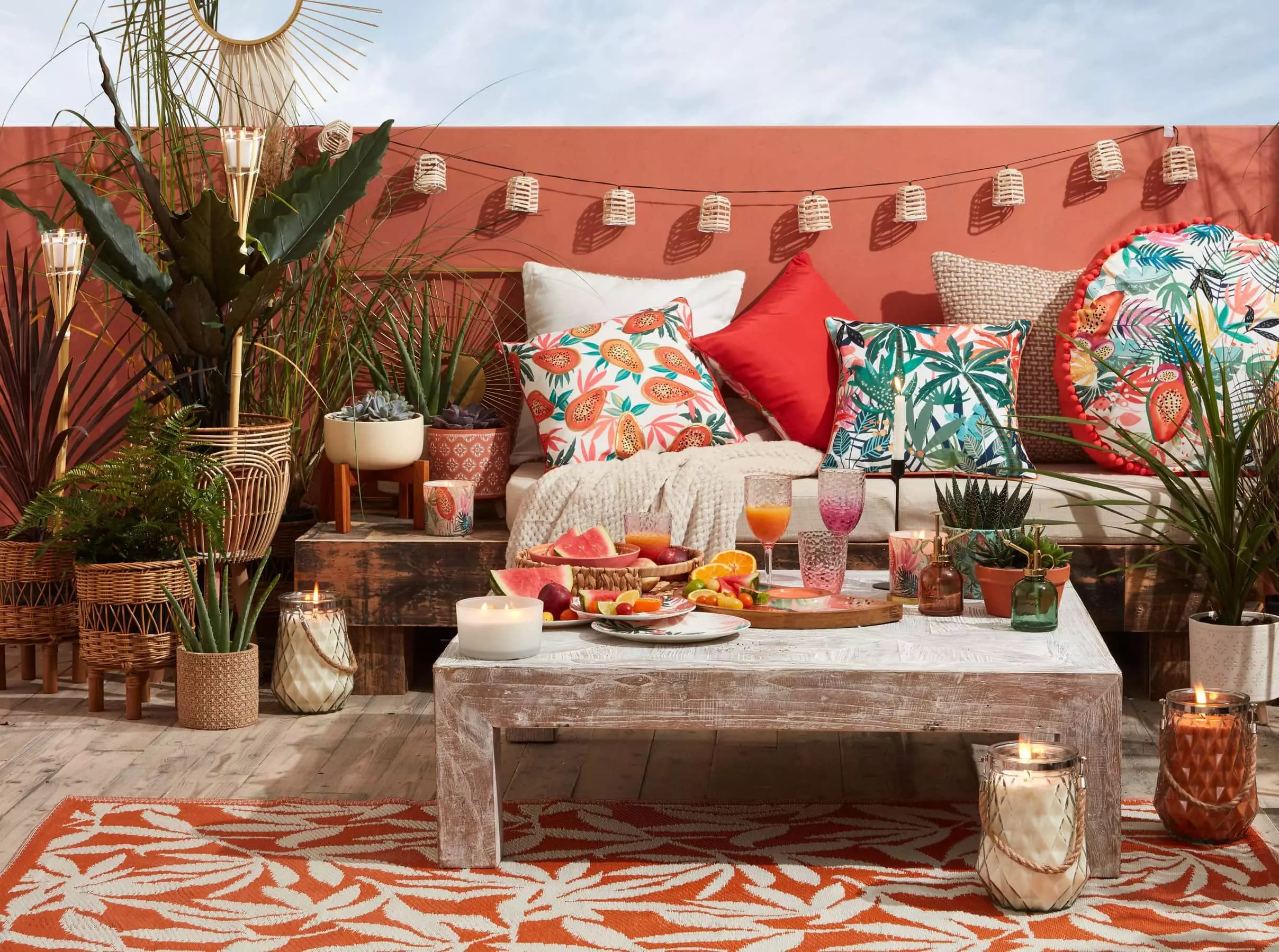 Orange painted garden wall with orange and white patterned outdoor rug. Chunky garden table, brightly colored cushions, and lots of plants
