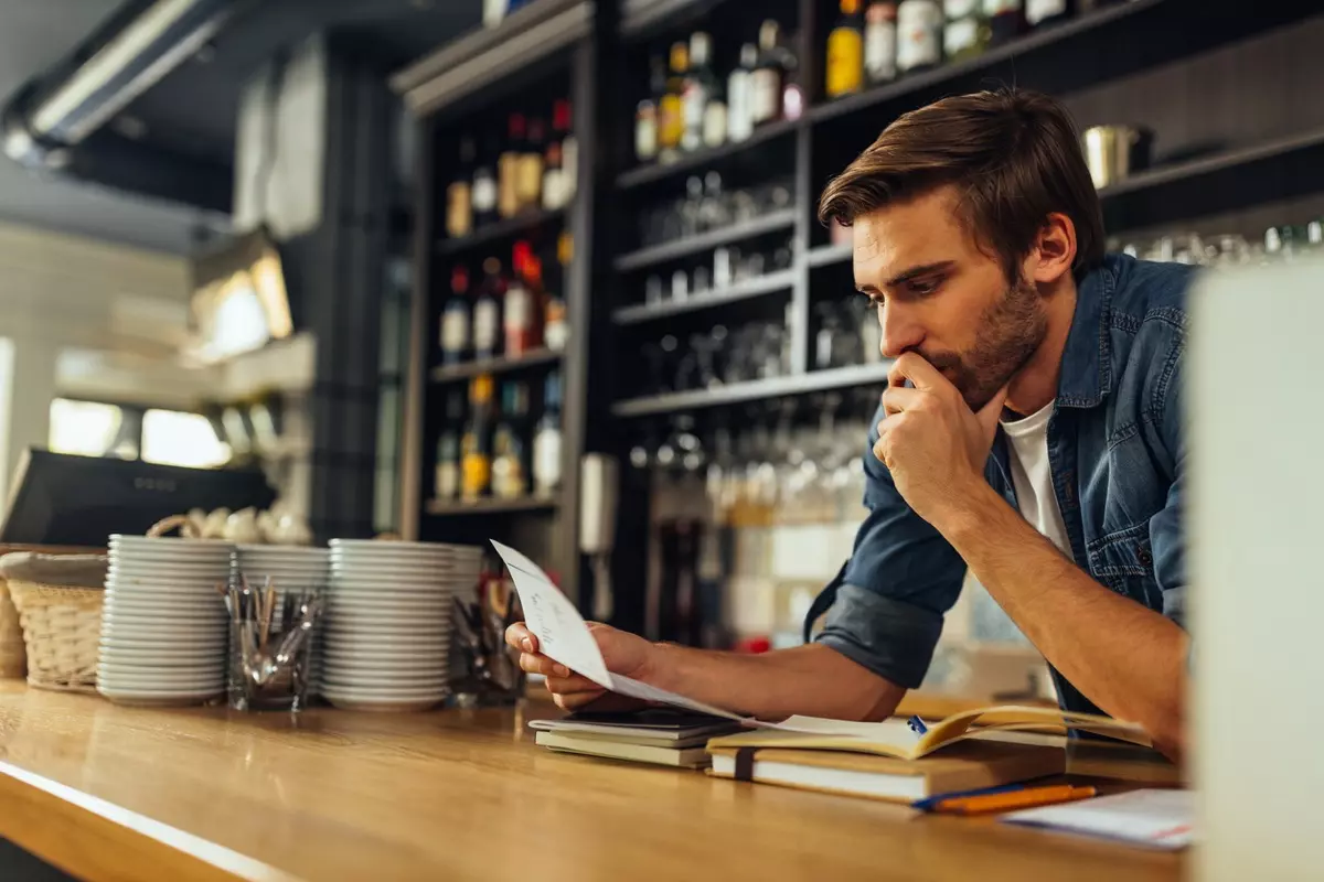 Owner of a restaurant checking financial business documentations while standing behind counter