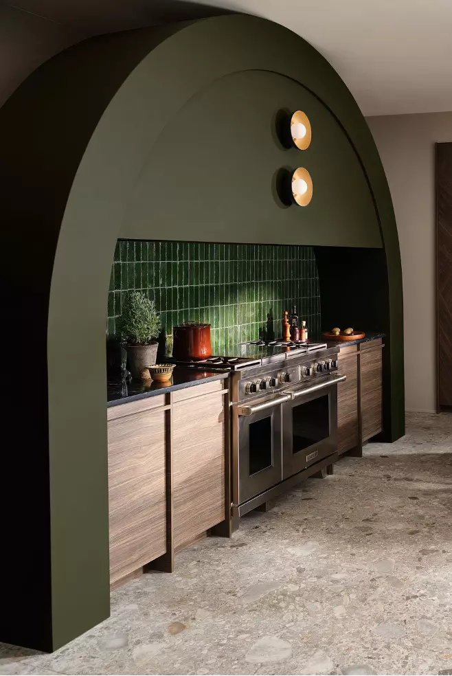 Statement range hood in dark olive-green with accent lights and a green tile backsplash, stone flooring