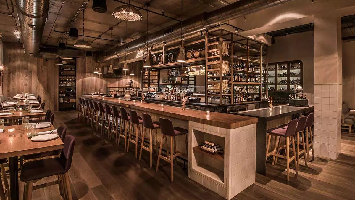 Seating area with large leather couches and chairs on the right and a bar on the left with a fireplace in the back at The Darling in Chicago, Illinois, USA