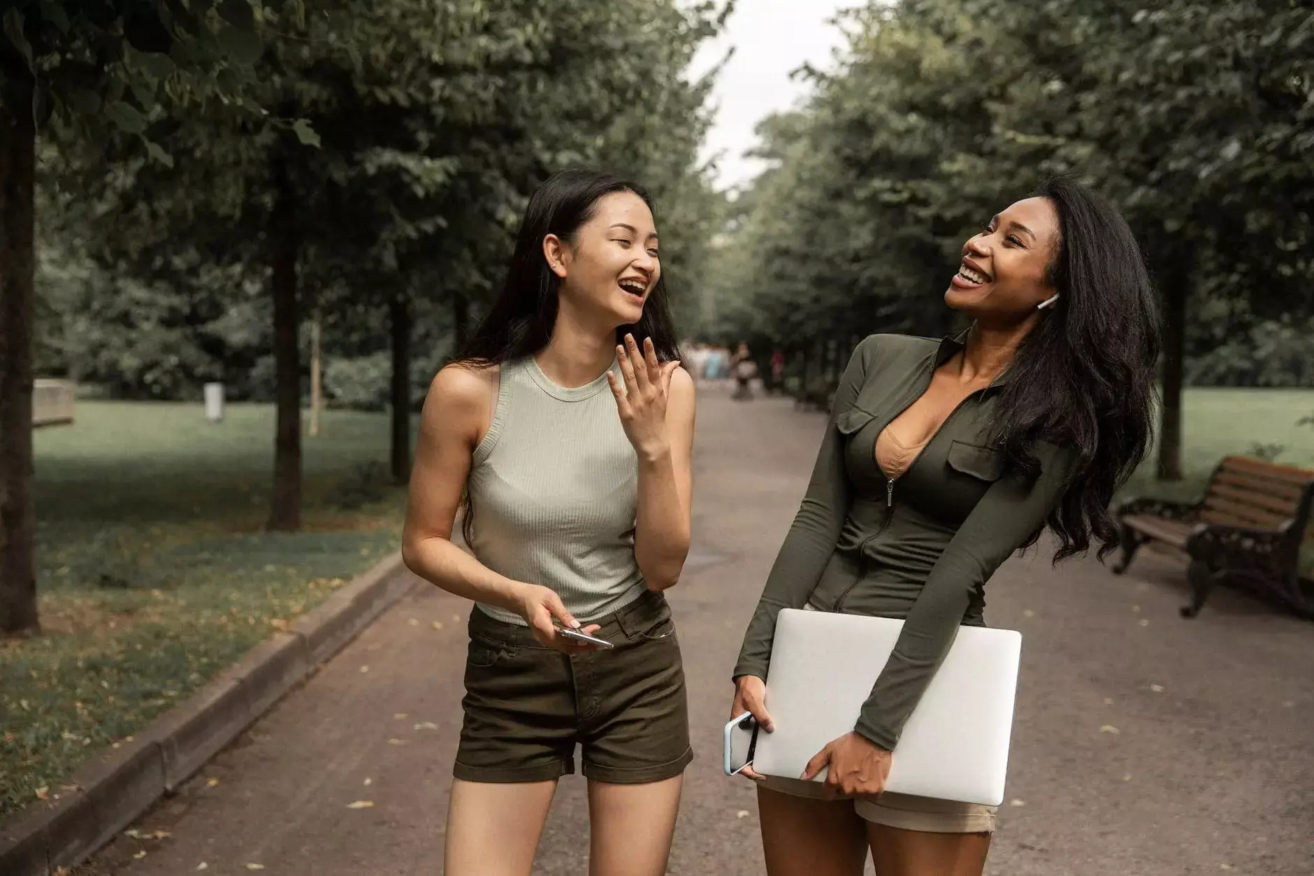 delighted young multiethnic women talking and laughing in green park