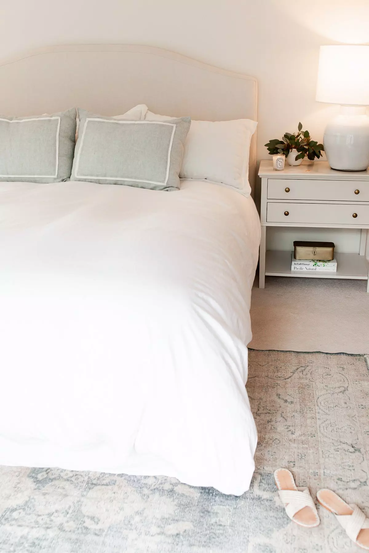 A bed with white bedding and a white nightstand, featuring a rug underneath.