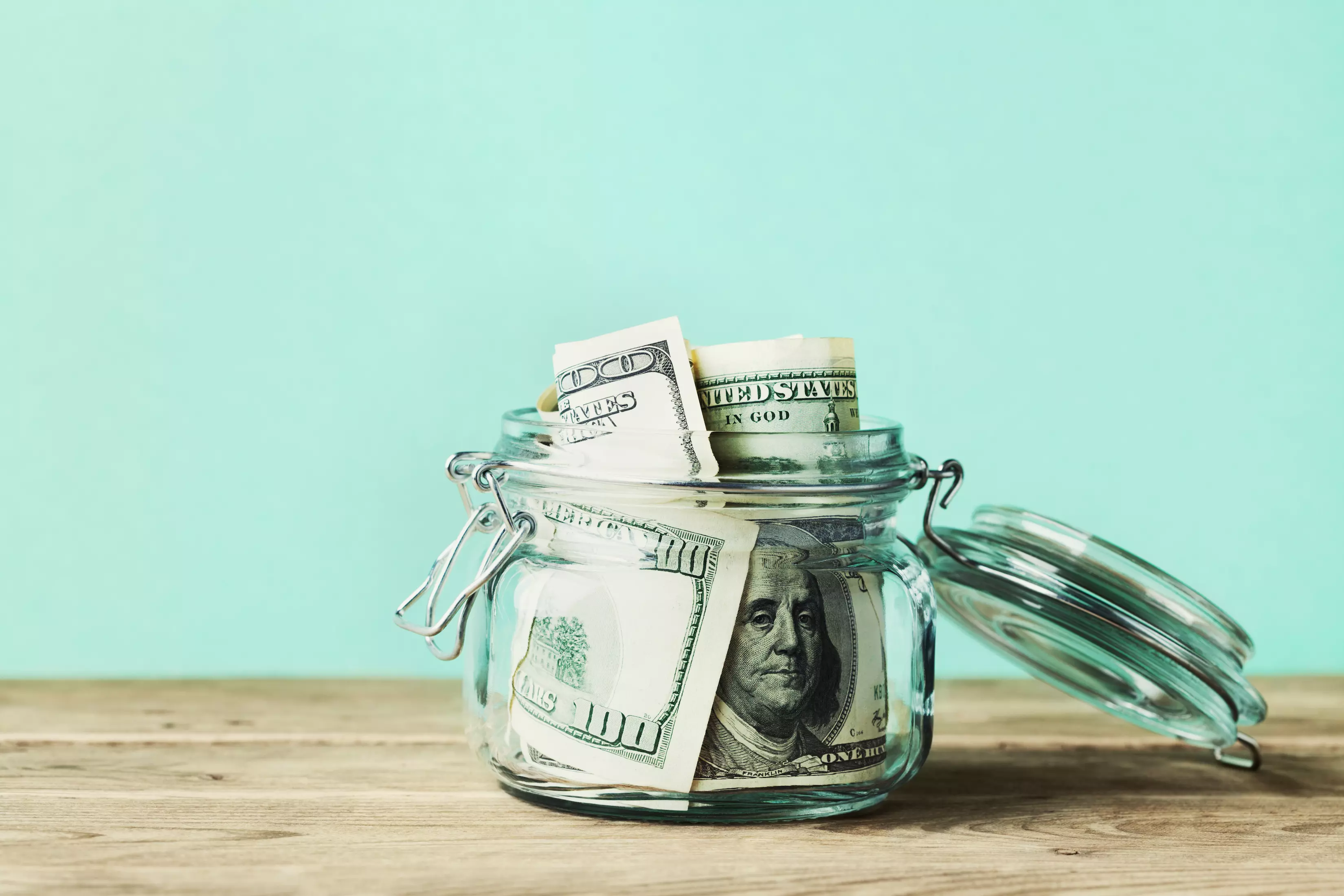 A mason jar of $100 bills sits on a counter